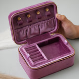 Purple jewelry case with gold accents held by a hand on a light background